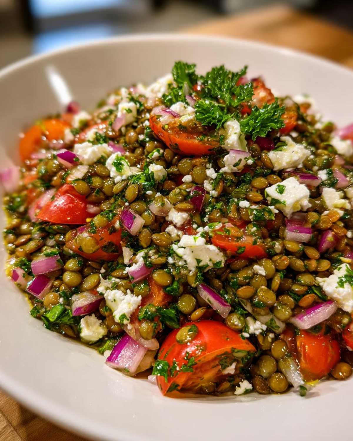 Close-up of a vibrant lentil salad featuring green lentils, cherry tomatoes, red onion, feta cheese, and parsley.