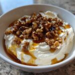 A white bowl filled with creamy whipped ricotta dip, drizzled with honey and topped with candied walnuts.