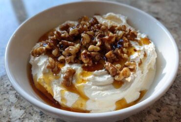 A white bowl filled with creamy whipped ricotta dip, drizzled with honey and topped with candied walnuts.
