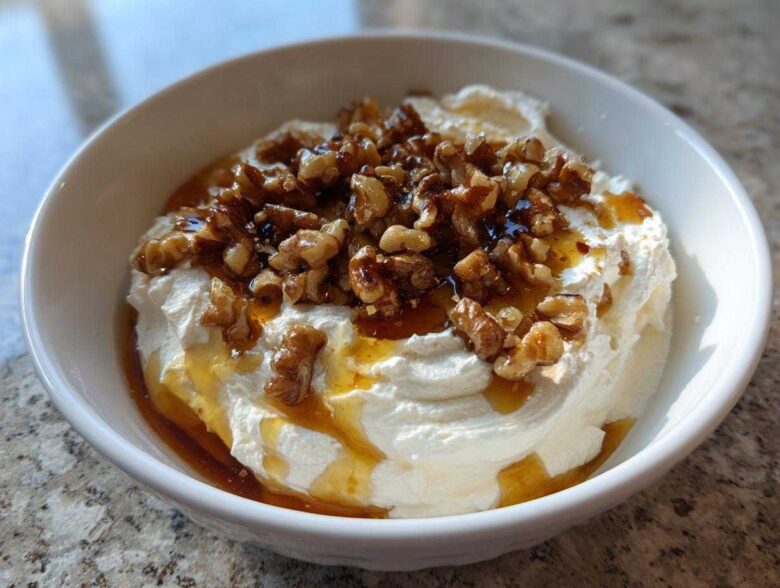 A white bowl filled with creamy whipped ricotta dip, drizzled with honey and topped with candied walnuts.