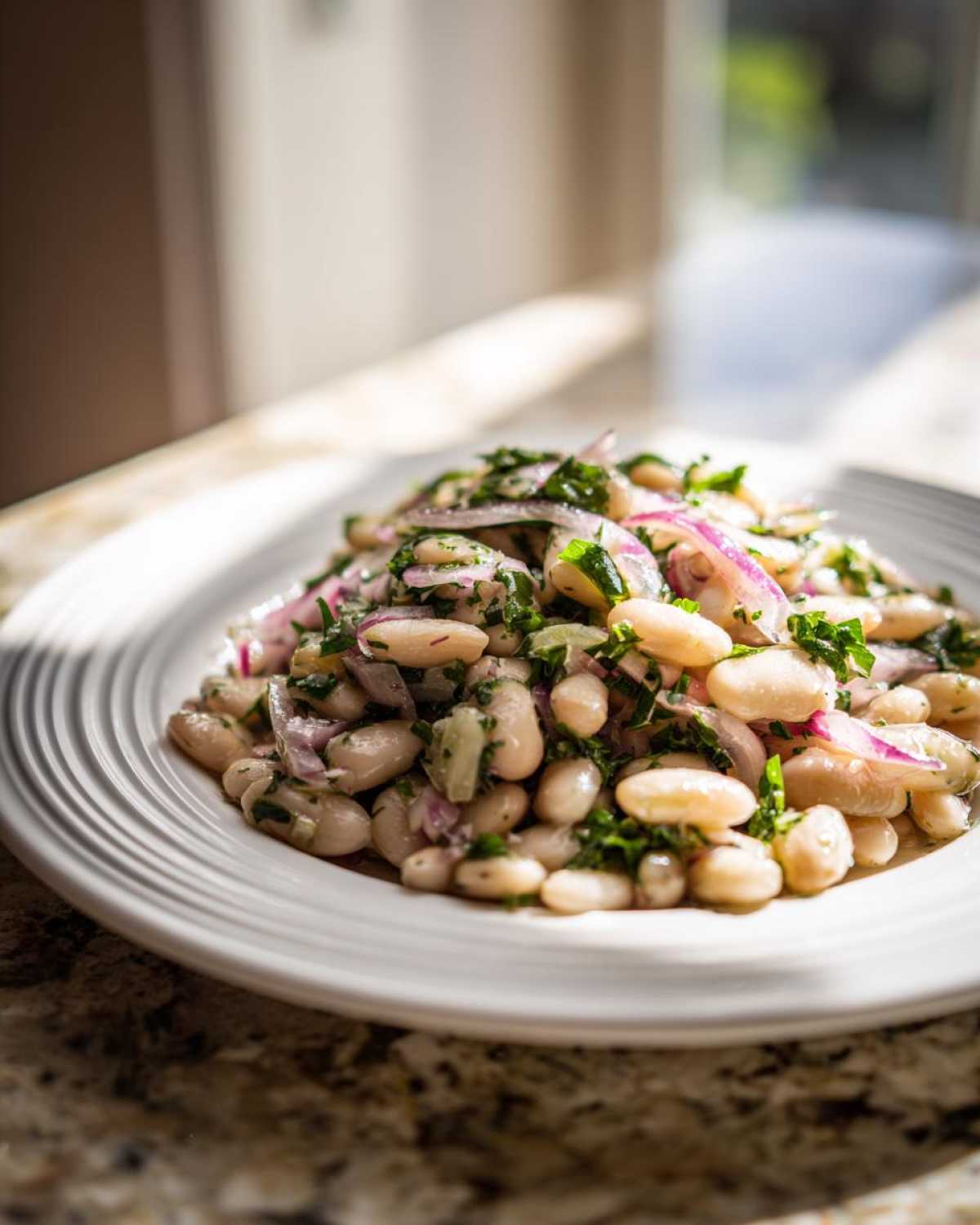 A close-up serving of bright white bean salad mixed with thinly sliced red onion and fresh green herbs.