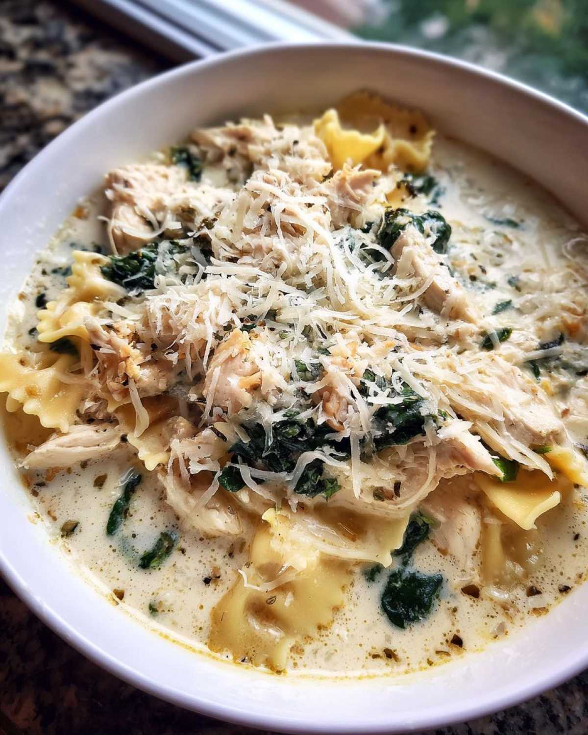 Close-up of a hearty bowl of white chicken lasagna soup topped with shredded chicken, spinach, and grated Parmesan cheese.