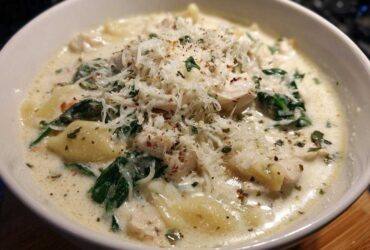 A close-up of a bowl of creamy white chicken lasagna soup, featuring pasta, chicken, spinach, and grated Parmesan cheese.