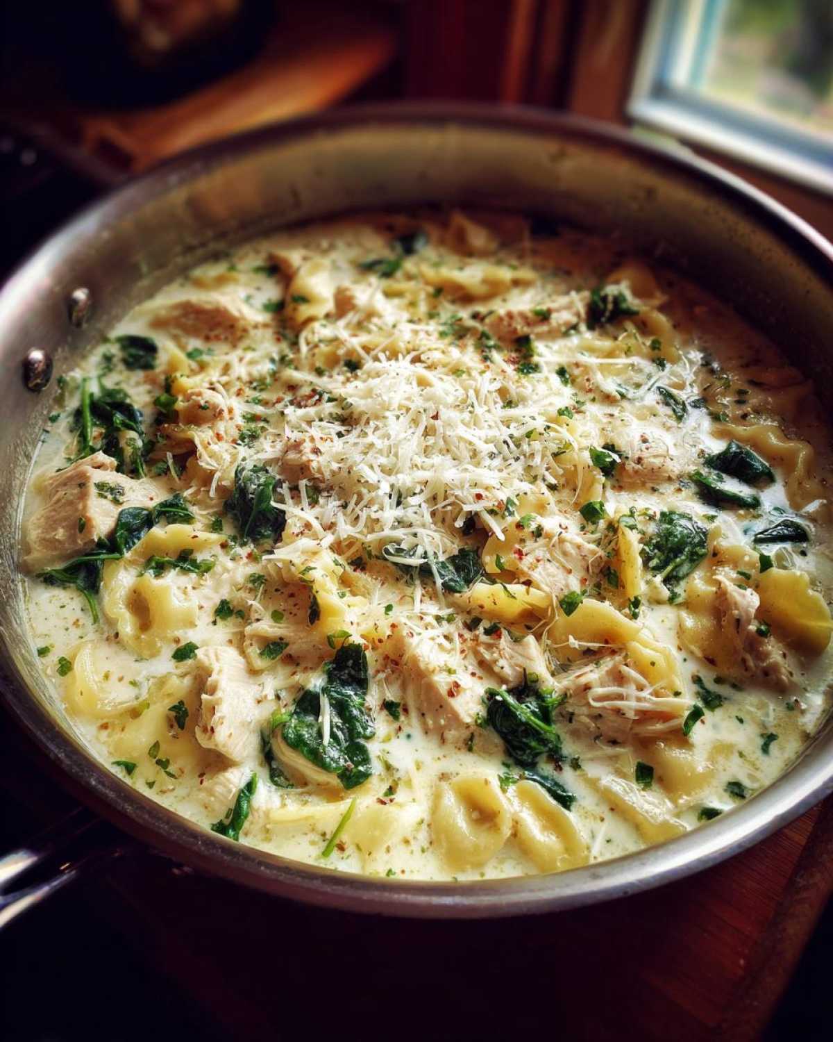 Close-up of creamy white chicken lasagna soup with tortellini, spinach, and grated Parmesan cheese in a stainless steel skillet.