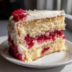 Close-up of a moist slice of white chocolate raspberry cake showing layers of white cake, raspberry filling, and white frosting.