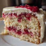 Close-up of a moist slice of white chocolate raspberry cake showing layers of white cake, raspberry filling, and white chocolate frosting.