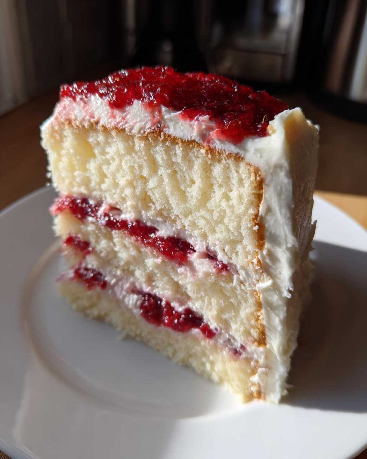 Close-up of a slice of white chocolate raspberry cake showing three layers of white cake, cream, and bright red raspberry filling.