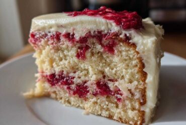 Close-up of a moist slice of white chocolate raspberry cake showing layers of white cake, raspberry filling, and white chocolate frosting.