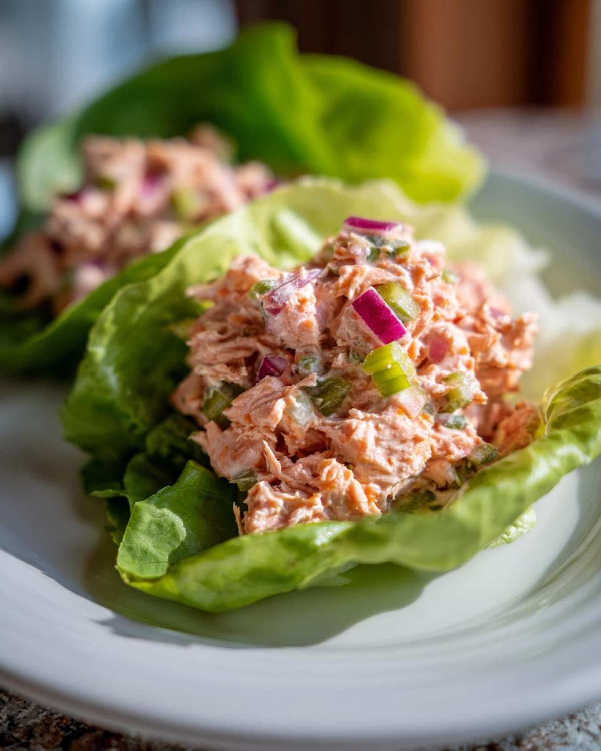Close-up of creamy salmon salad mixed with red onion and celery served in crisp lettuce cups.