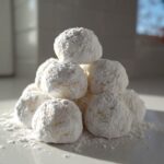 A mound of soft, round 3-ingredient cool whip cookies heavily dusted with powdered sugar on a white plate.