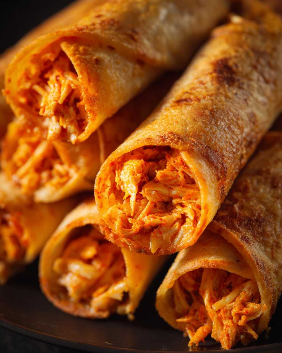 Close-up of several golden brown Air Fryer Crispy Buffalo Chicken Taquitos stacked, showing the shredded orange buffalo chicken filling.