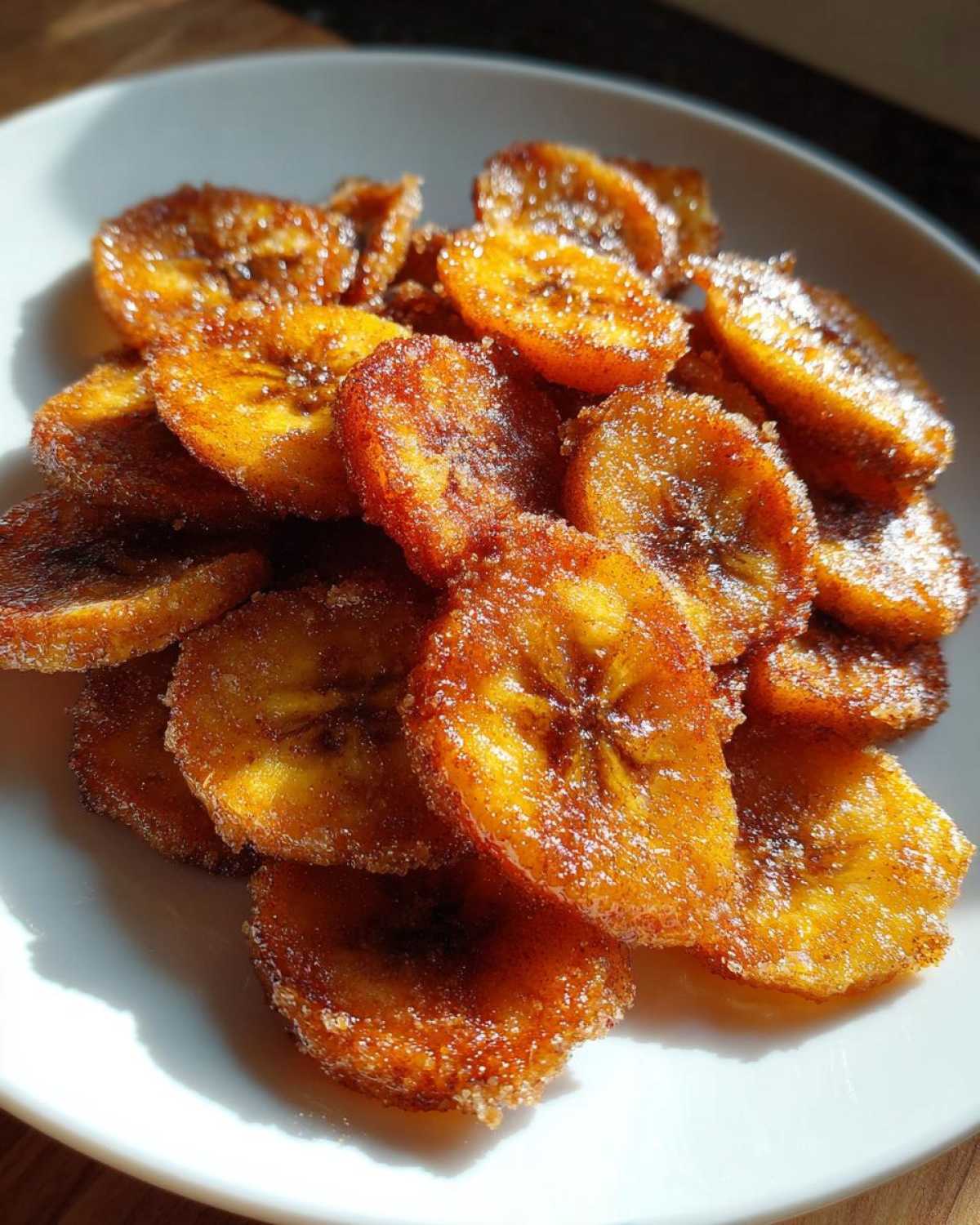 Close-up of golden brown Air Fryer Crispy Cinnamon Sugar Banana Chips piled on a white plate.
