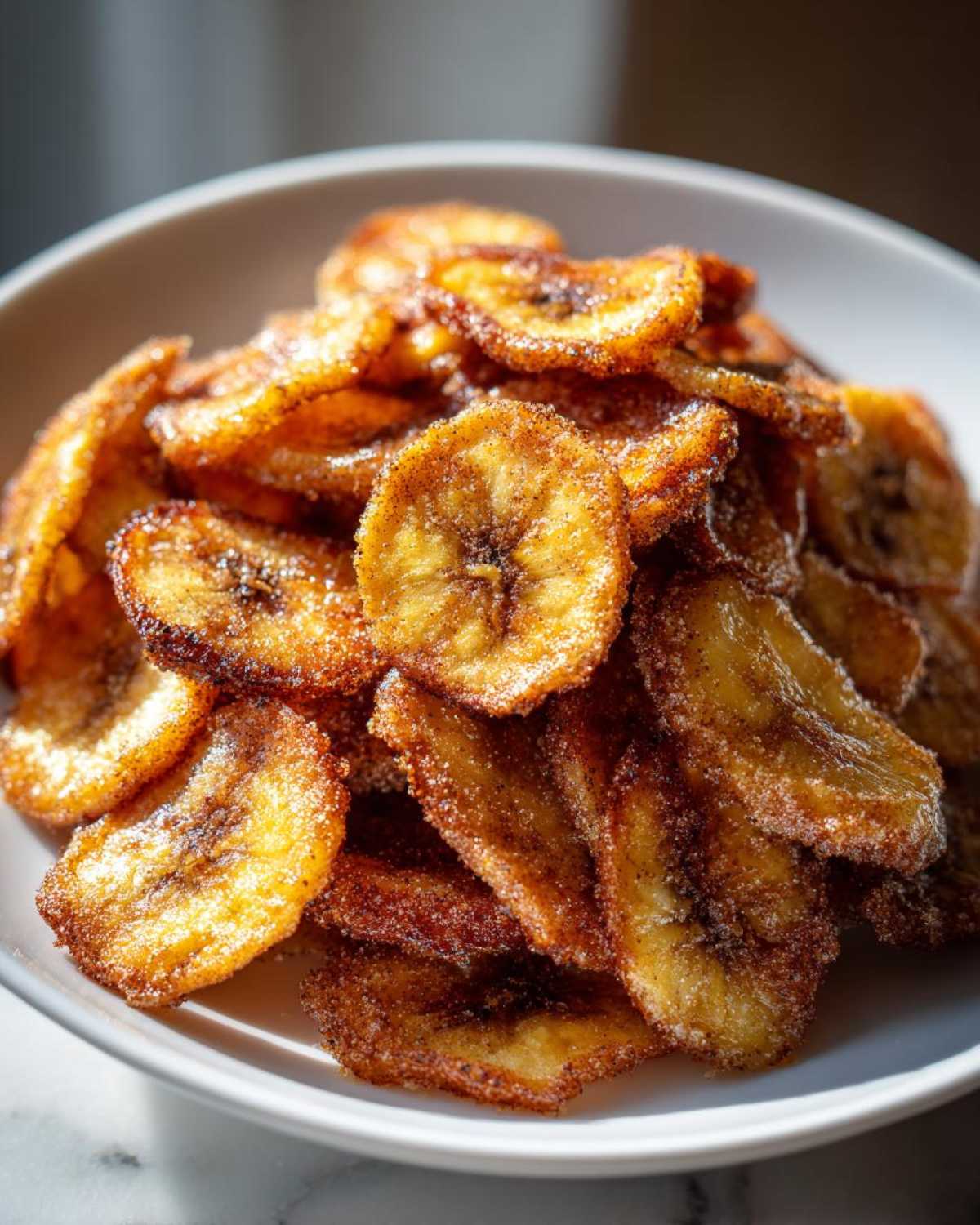 A close-up of a white bowl filled with golden brown Air Fryer Crispy Cinnamon Sugar Banana Chips.