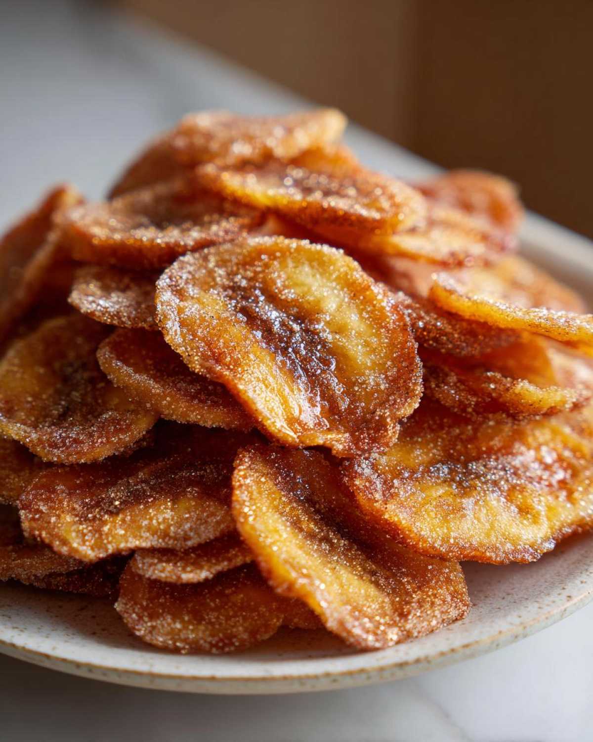 A close-up of a pile of golden brown Air Fryer Crispy Cinnamon Sugar Banana Chips dusted with sugar.