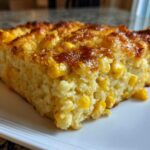 Close-up of a golden-brown slice of moist corn casserole filled with bright yellow corn kernels.
