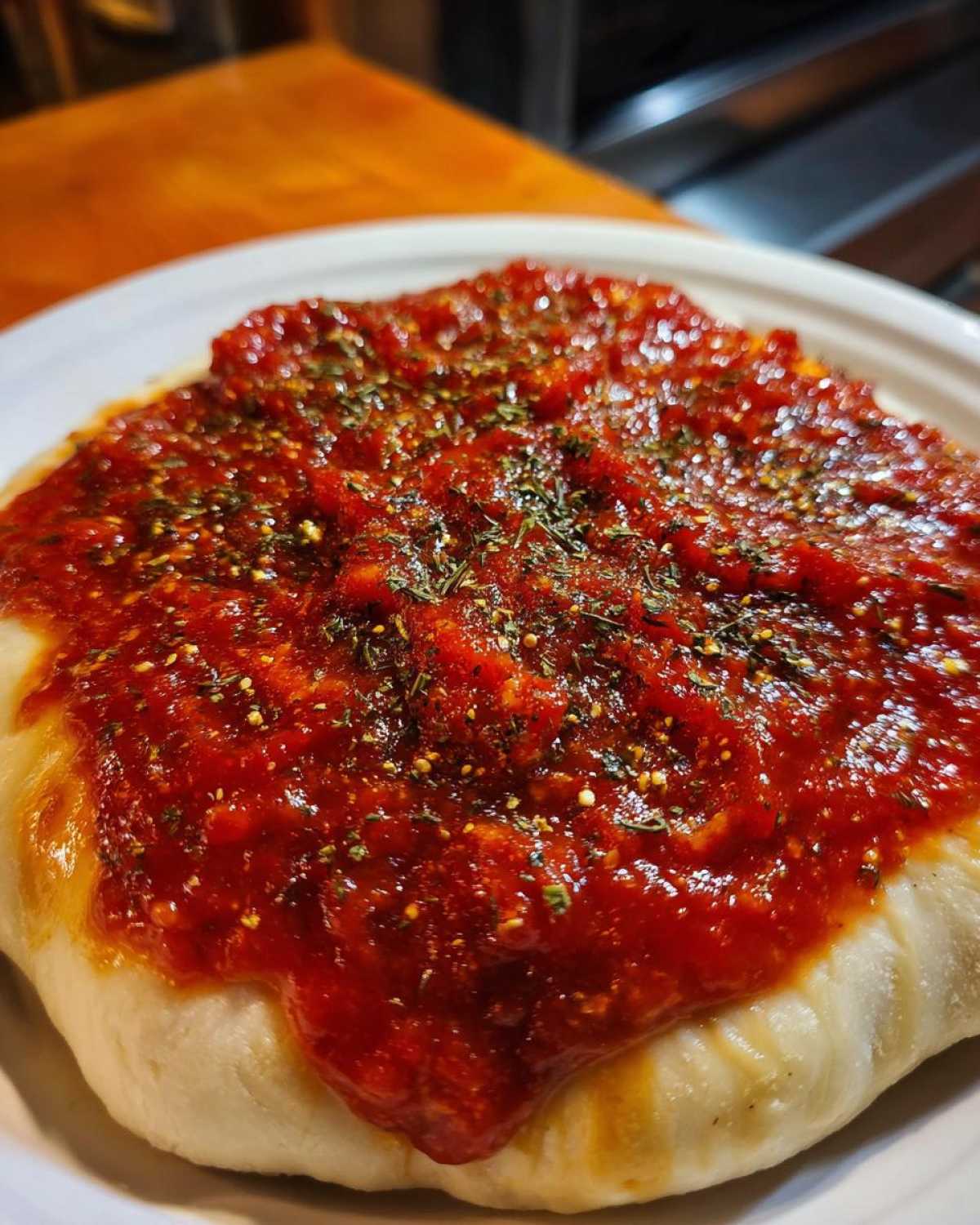 Close-up of thick, vibrant red pizza sauce generously spread over raw dough and topped with dried herbs.