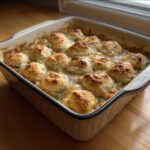 A close-up of a bubbling chicken pot pie casserole topped with golden-brown biscuits, fresh from the oven.