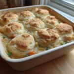 A square baking dish filled with bubbling chicken pot pie casserole topped with golden brown biscuits.