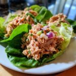 Close-up of healthy salmon salad mixture served inside fresh green lettuce cups on a white plate.