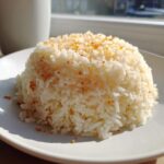 A mound of fluffy white butter rice topped with crispy golden garlic bits, served on a white plate.