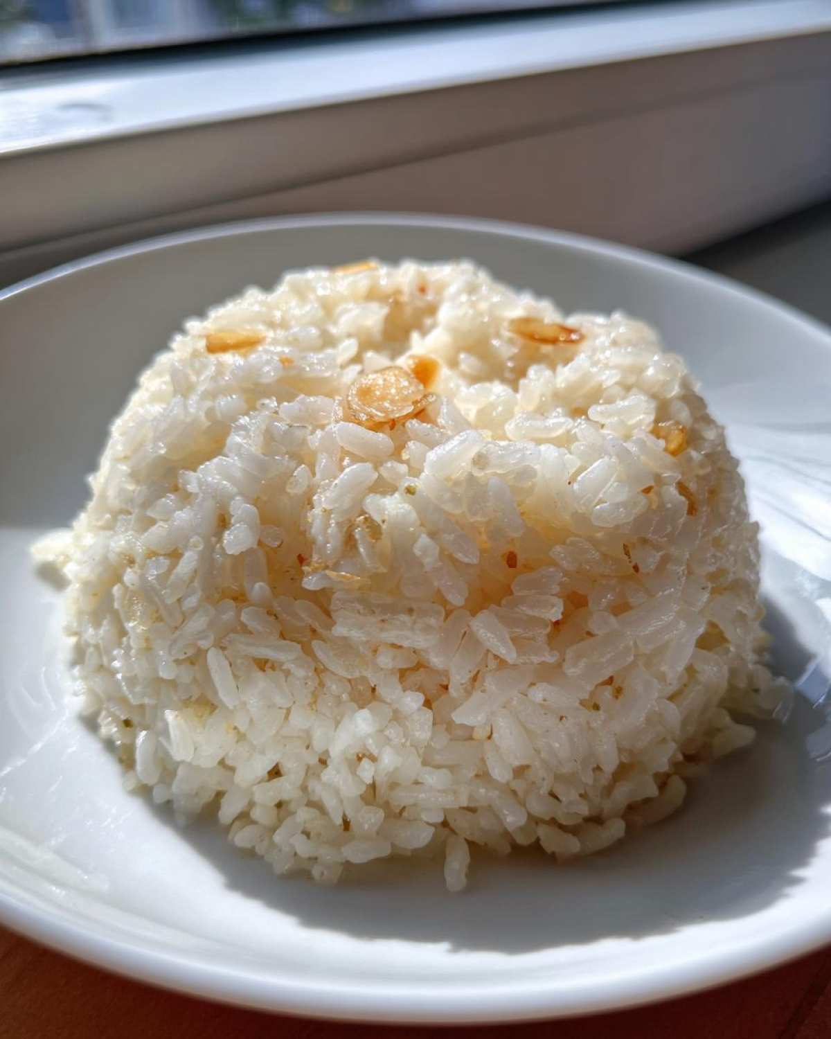 A mound of fluffy white butter rice topped with crispy fried garlic pieces, served on a white plate.