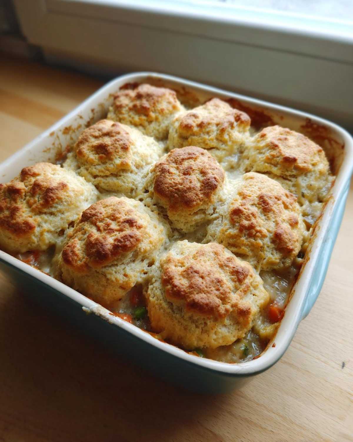 A square baking dish filled with bubbling chicken pot pie casserole topped with golden brown biscuits.