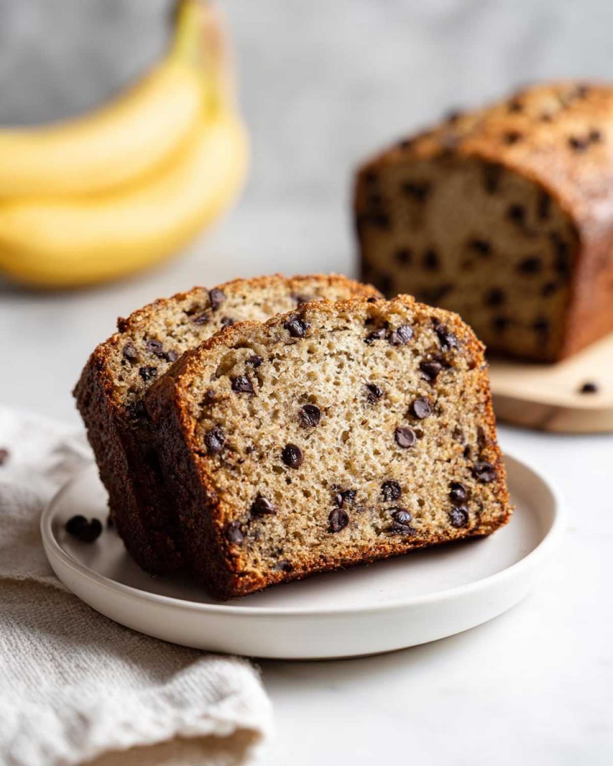 Two thick slices of moist vegan banana bread studded with chocolate chips, served on a white plate.
