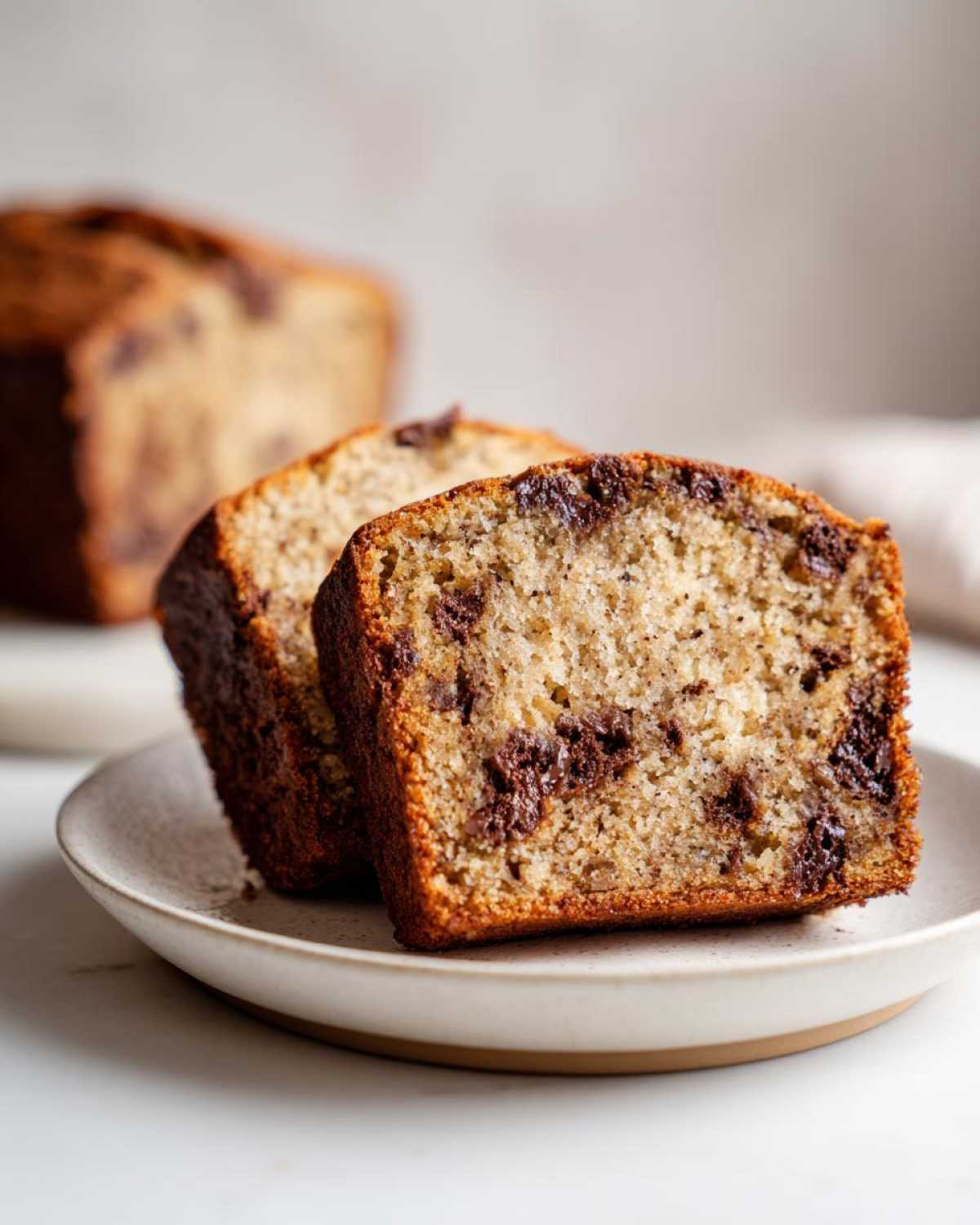 Two thick slices of moist vegan banana bread loaded with melted chocolate chips, served on a small plate.