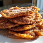 Close-up of a stack of four golden-brown buñuelos generously coated in cinnamon sugar.