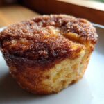 A close-up, featured shot of one perfectly baked cinnamon sugar french toast muffins with a crunchy, sugary topping.