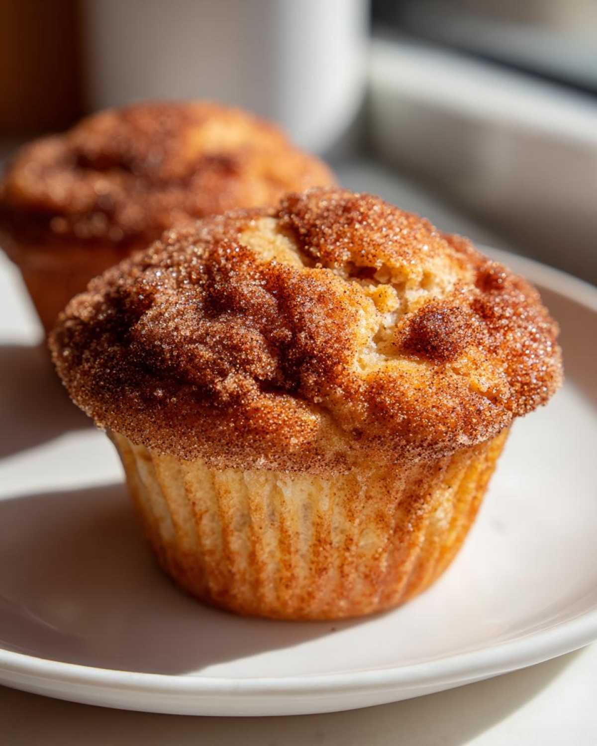 A close-up of a freshly baked cinnamon sugar french toast muffin sitting on a white plate.