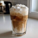 A tall glass of Copycat Starbucks Iced White Chocolate Mocha topped with whipped cream.