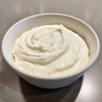 A close-up of thick, white, creamy horseradish sauce swirled in a small white bowl.