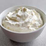 A close-up of fluffy, white creamy horseradish sauce swirled high in a small white bowl.