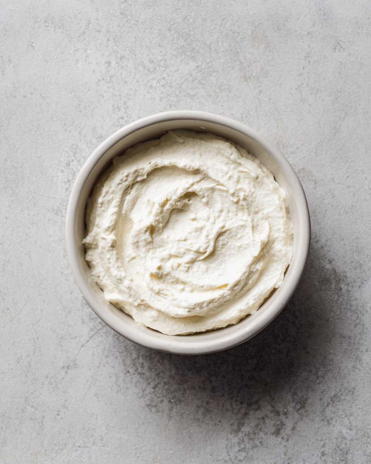 Overhead view of a small bowl filled with thick, white, creamy horseradish sauce against a gray background.