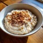 A close-up of a bowl of creamy rice pudding recipe generously dusted with ground cinnamon.