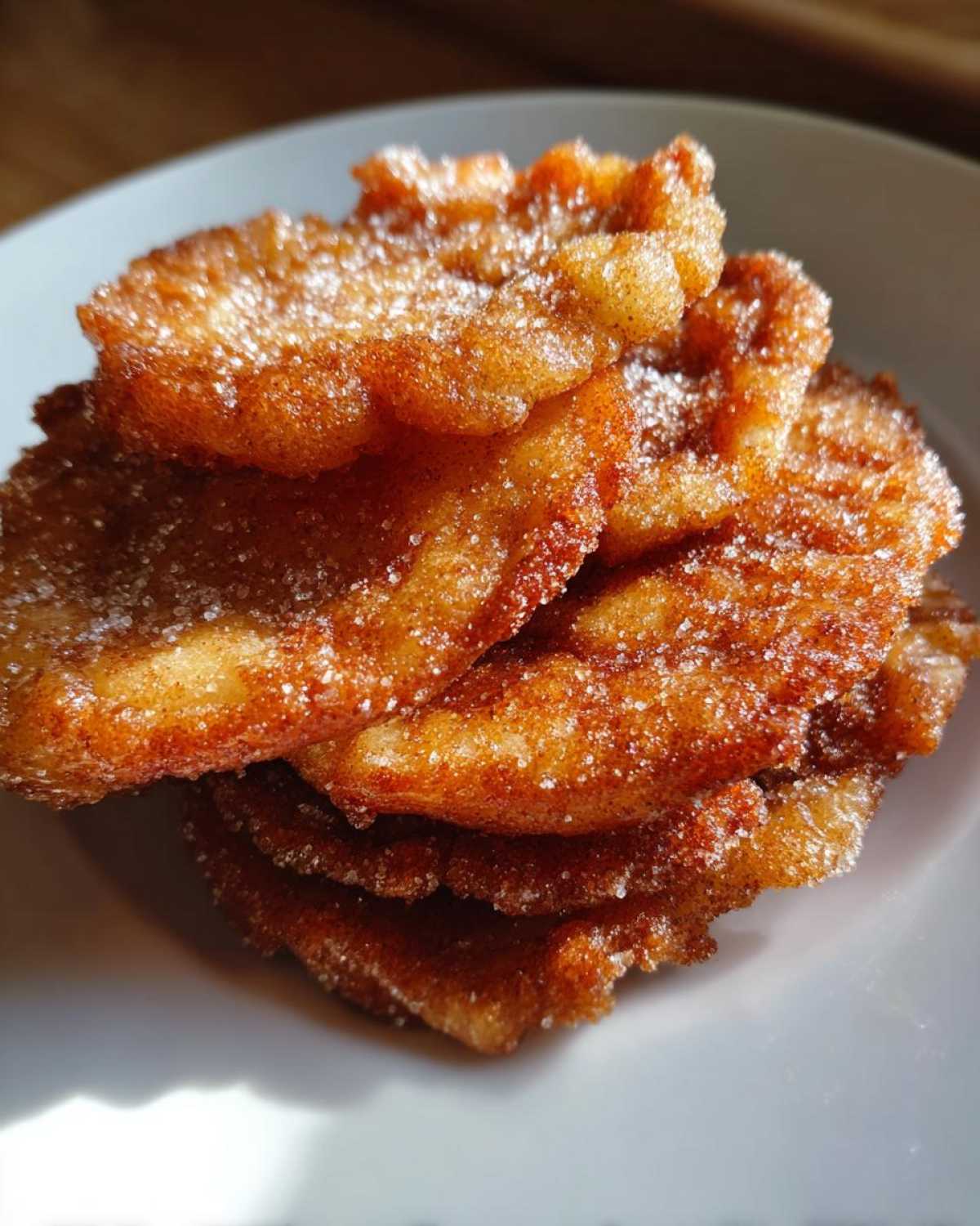 Close-up of a stack of golden brown, crispy buñuelos generously coated in cinnamon sugar.