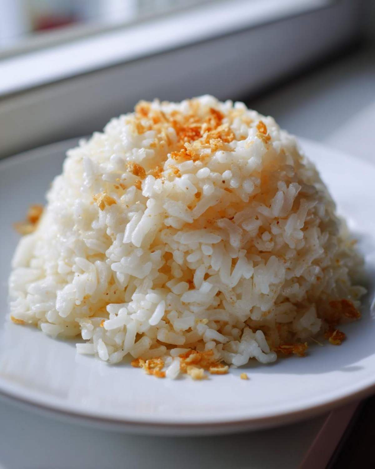 A perfectly molded mound of white butter rice topped with crispy, browned garlic bits on a white plate.