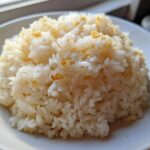 A close-up of a mound of fluffy, white butter rice served on a white plate, lightly seasoned.