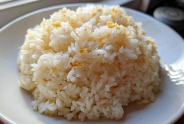 A close-up of a mound of fluffy, white butter rice served on a white plate, lightly seasoned.