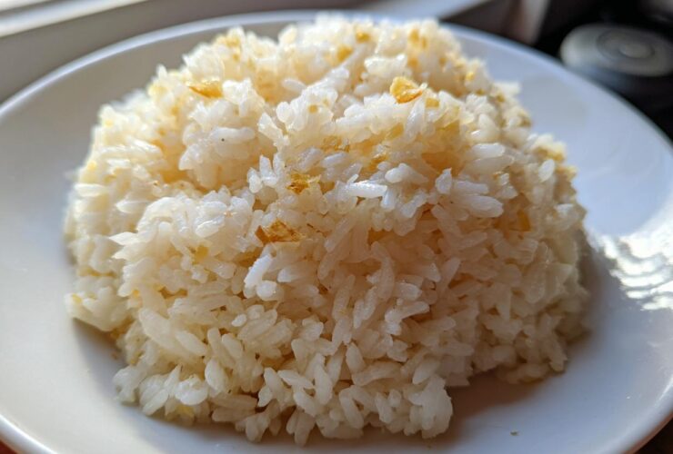 A close-up of a mound of fluffy, white butter rice served on a white plate, lightly seasoned.