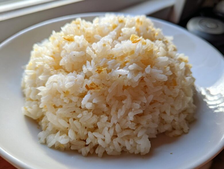 A close-up of a mound of fluffy, white butter rice served on a white plate, lightly seasoned.
