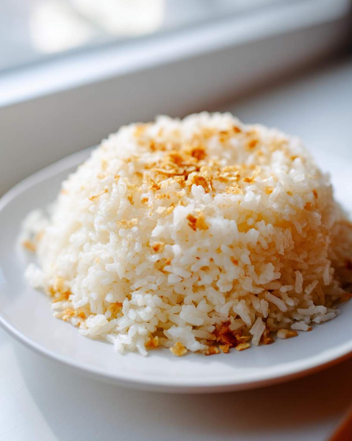 A mound of fluffy white butter rice served on a white plate, topped with golden crispy garlic.