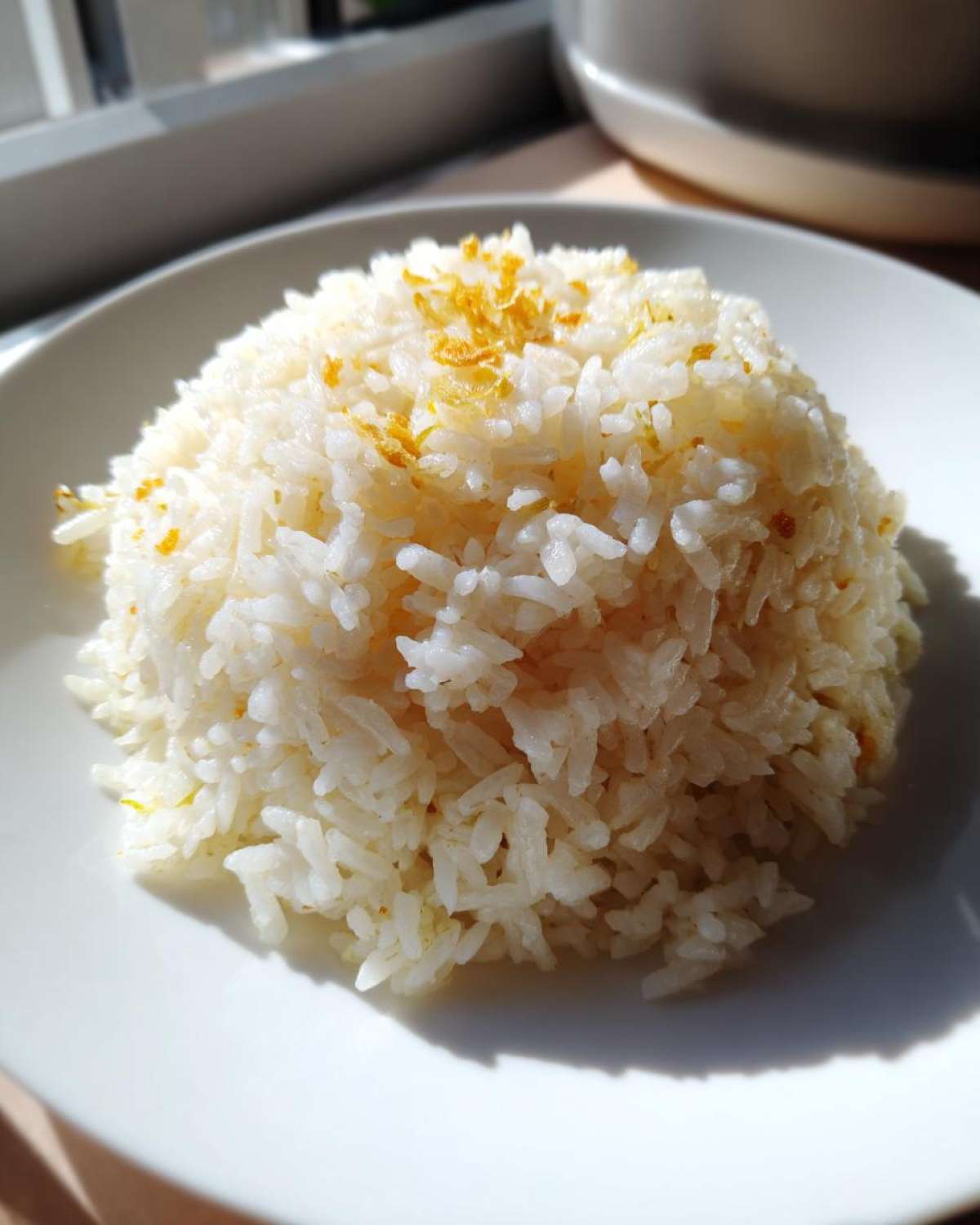 A mound of fluffy white butter rice topped with golden crispy garlic bits on a white plate.
