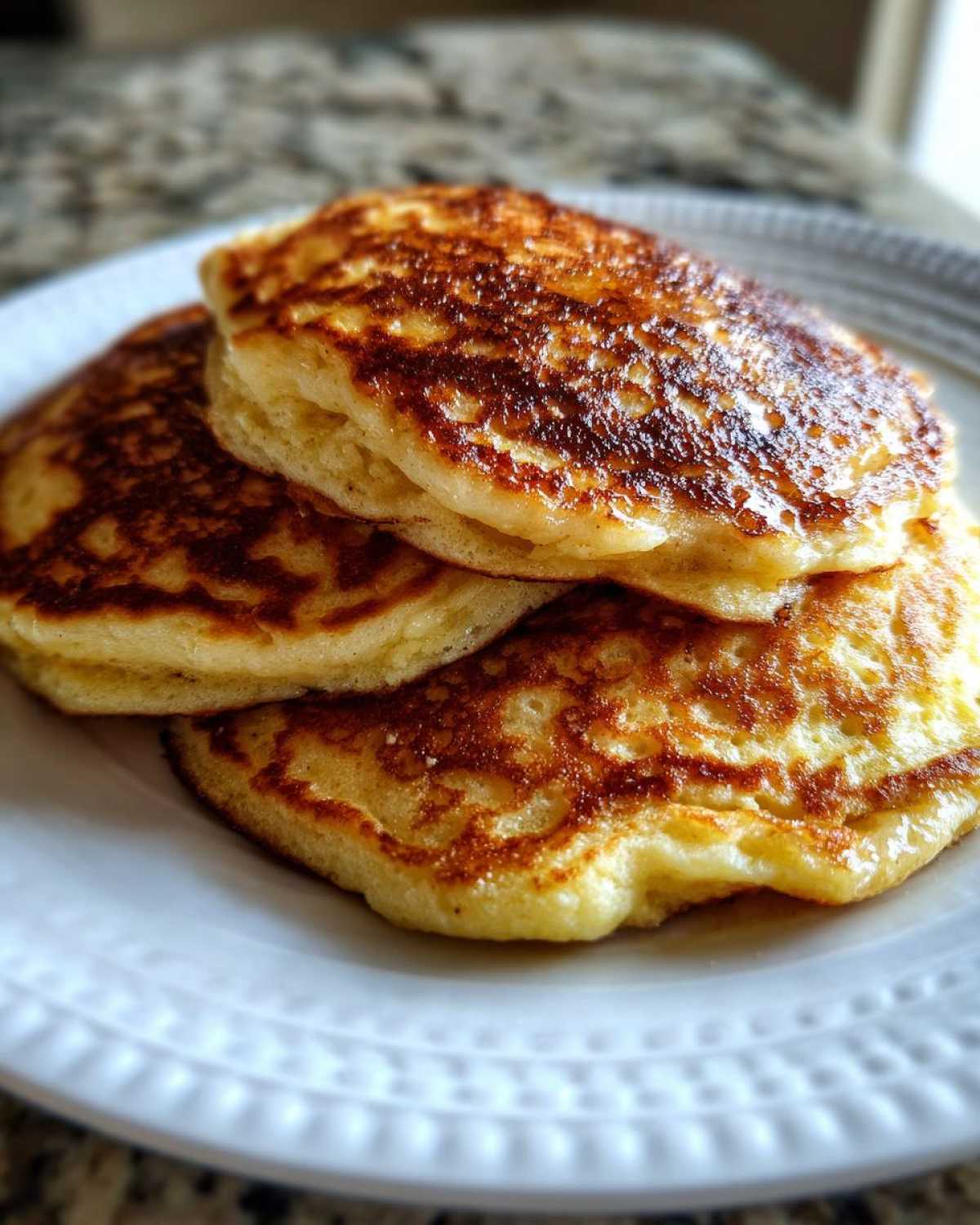 A close-up stack of three fluffy coconut flour pancakes with golden-brown, lacy tops served on a white plate.