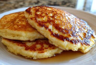 A stack of three fluffy coconut flour pancakes drizzled generously with golden syrup on a white plate.