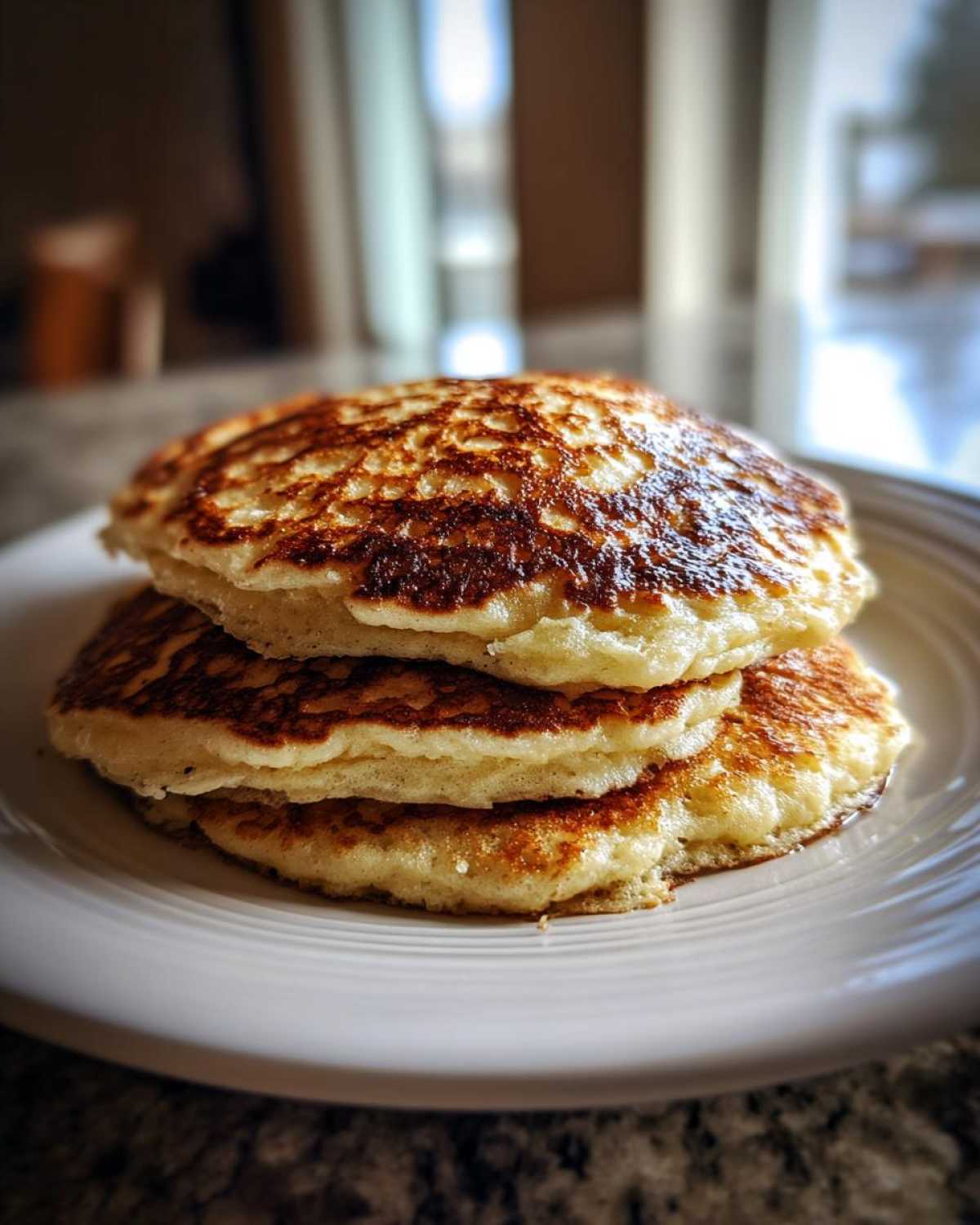 A stack of three golden-brown coconut flour pancakes resting on a white plate.