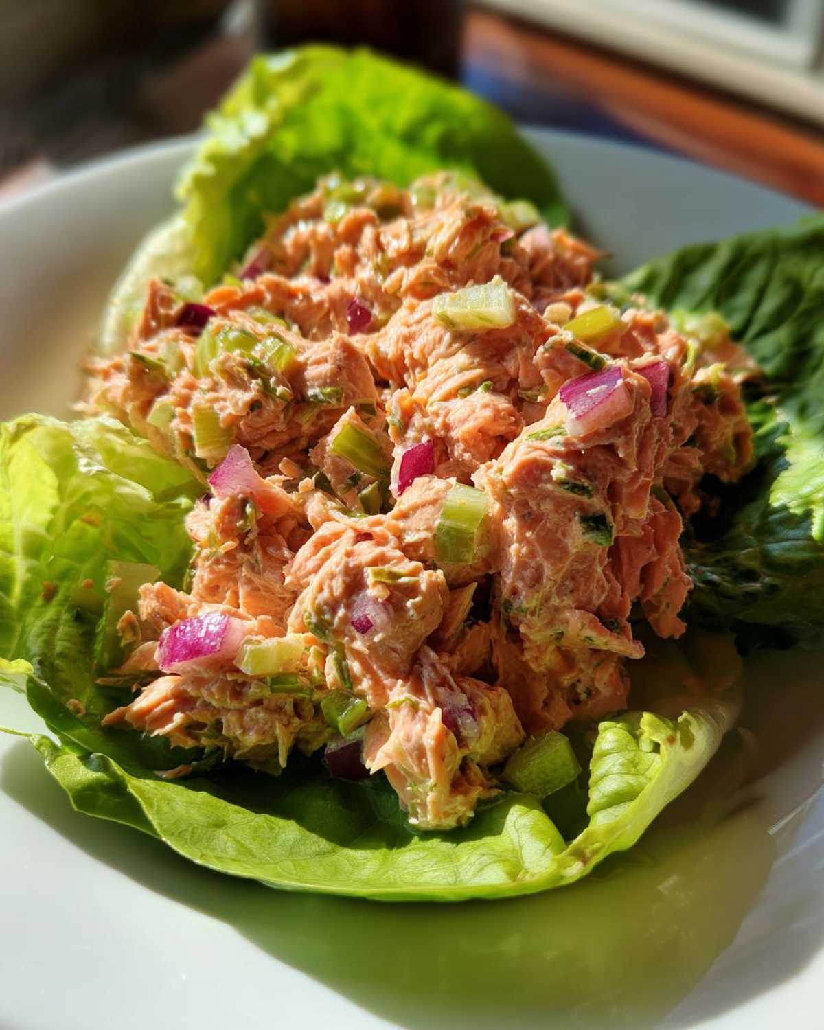 A close-up of fresh salmon salad mixed with celery and red onion, served in bright green lettuce cups.