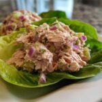 Close-up of fresh salmon salad mixed with red onion and celery served in bright green lettuce cups.