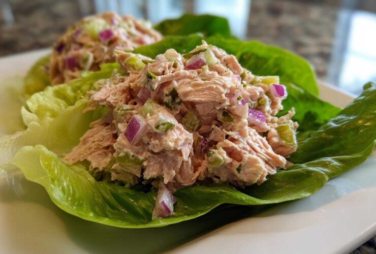 Close-up of fresh salmon salad mixed with red onion and celery served in bright green lettuce cups.